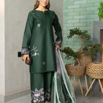 Woman in a green traditional outfit with floral patterns, holding a dupatta, against a light green tiled wall.